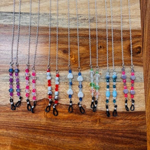 May include: A set of 10 beaded eyeglass chains with silver chains and various colored beads, including purple, pink, red, white, blue, green, and gray. The chains have black rubber stoppers on the ends.