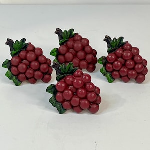 Può includere: Quattro grappoli d'uva decorativi. Ogni grappolo presenta un colore rosso intenso con foglie verdi e un gambo marrone. L'uva è rotonda e fitta, creando un aspetto realistico.