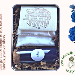 May include: A metal tin with a clear glass bottle labeled "Indigo" and three white packets. The tin is filled with brown packing material. The text on the tin reads "Pre-measured ingredients to create a large vat of indigo to dye natural fabrics, yarn or fibers."