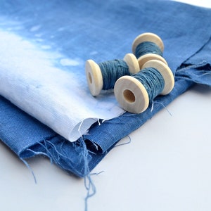 May include: Four spools of blue thread wound around wooden bobbins, sitting on top of a folded piece of blue fabric.
