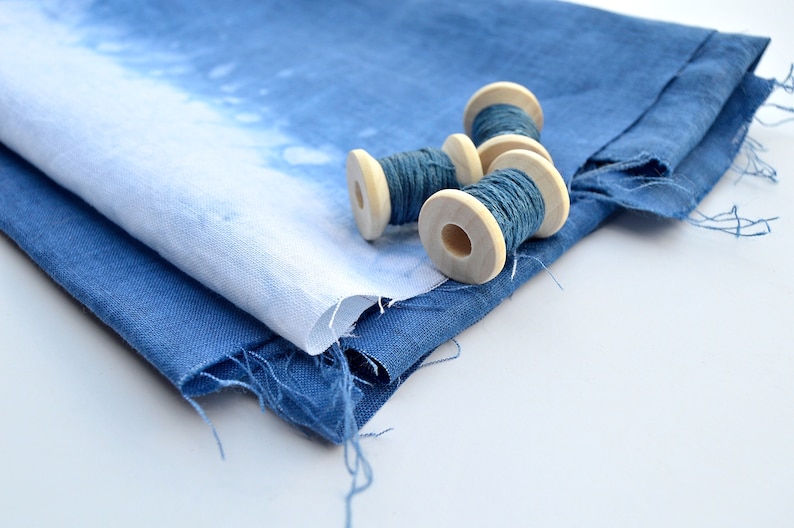 May include: Four spools of blue thread wound around wooden bobbins, sitting on top of a folded piece of blue fabric.