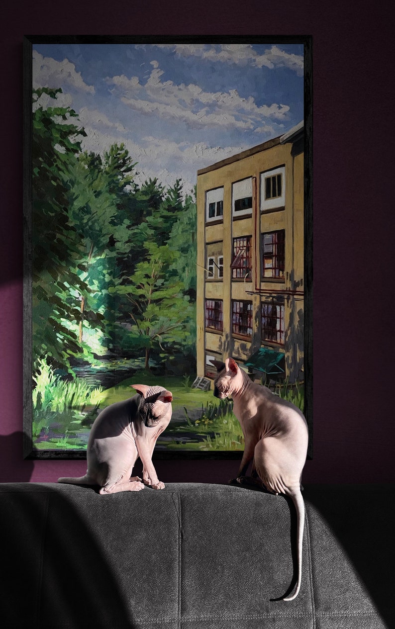 May include: Two hairless cats sit on a dark gray couch in front of a framed painting of a building with a green forest behind it. The painting has a blue sky with white clouds.