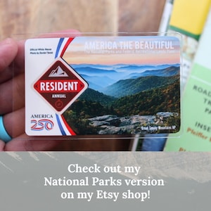 May include: A clear plastic America the Beautiful National Parks Pass. The pass features a scenic view of the Great Smoky Mountains and the text "RESIDENT ANNUAL". The pass also has the text "AMERICA 250".