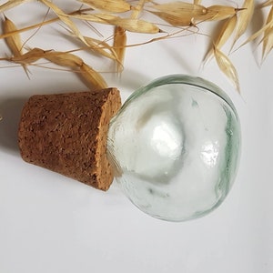 May include: A clear glass bottle with a cork stopper. The bottle is round and has a smooth surface. The cork is brown and has a rough texture.