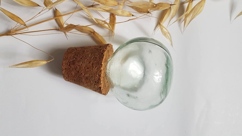 May include: A clear glass bottle with a cork stopper. The bottle is round and has a smooth surface. The cork is brown and has a rough texture.