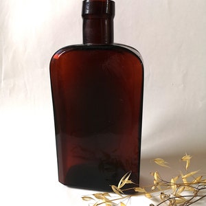 Peut inclure: Une bouteille en verre brun foncé de forme rectangulaire arrondie avec un col court. La bouteille est vide et a une surface lisse.