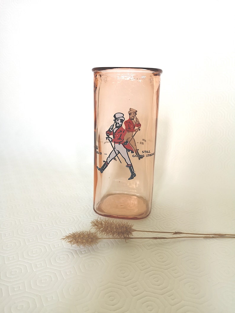 Peut inclure: Un verre en verre rose avec une image imprim&eacute;e de deux hommes en v&ecirc;tements rouge et blanc marchant avec des b&acirc;tons de marche. Le texte "Still Going Strong" est imprim&eacute; sur le verre.