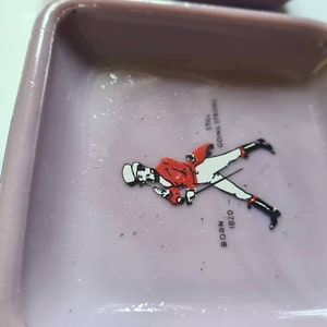 K&ouml;nnte beinhalten: Ein lilafarbener Aschenbecher aus Keramik mit einem Johnnie Walker-Logo, das einen Mann in einer roten Jacke auf einem Pferd zeigt. Das Logo enth&auml;lt auch den Text "Born 1820" und "Still Going Strong".