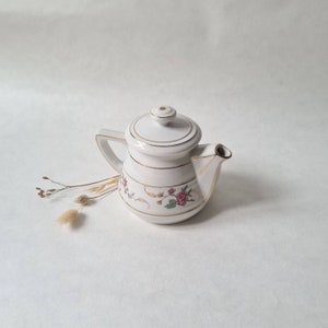 Peut inclure: Théière en porcelaine blanche avec un motif floral et des accents dorés. La théière a un couvercle et un bec.