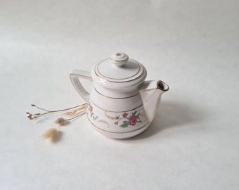 May include: White porcelain teapot with a floral design and gold accents. The teapot has a lid and a spout.