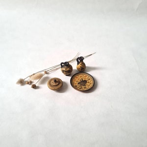 Peut inclure: Un ensemble de quatre pièces de poterie grecque miniatures, comprenant deux petites amphores, un petit pot à couvercle et une petite assiette avec un motif noir et jaune d'un oiseau. Les pièces sont sur un fond blanc.