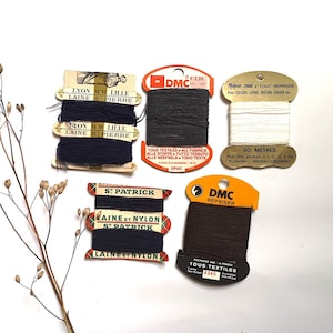 May include: Assortment of six spools of thread in various colors, including black, brown, and white. The spools are labeled with the brand name "DMC" and the text "Repriser" and "Tous Textiles".