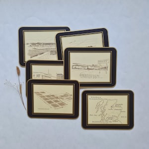 Puede incluir: Un juego de cinco manteles individuales rectangulares con centro color crema y borde negro grueso. Cada mantel presenta una ilustración única en tinta marrón de una destilería o un mapa de Escocia, con texto que identifica las ubicaciones.