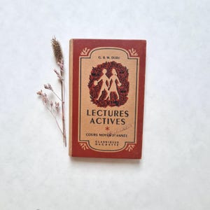 May include: A vintage red and cream book titled "Lectures Actives" with the text "Cours Moyen 2e Annee" and "Classiques Hachette". The cover features a black and white illustration of two children walking.