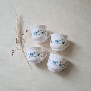 May include: Four white ceramic teacups with blue floral designs. The cups have a scalloped rim and a handle.