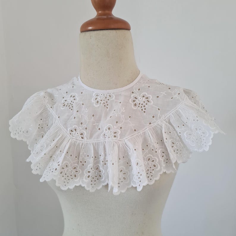 May include: White cotton lace collar with a scalloped edge and delicate floral embroidery.