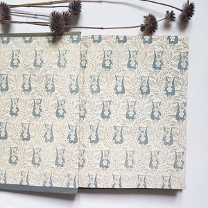 May include: A vintage book with a blue and white floral pattern on the cover. The book is closed and lying flat on a white surface.