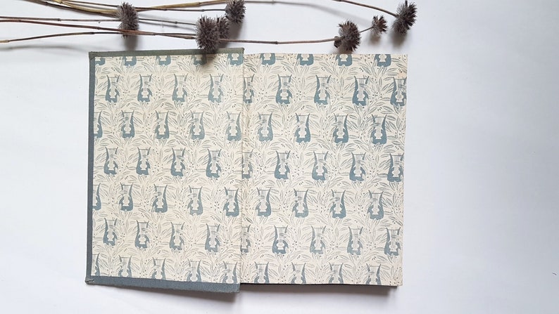 May include: A vintage book with a blue and white floral pattern on the cover. The book is closed and lying flat on a white surface.