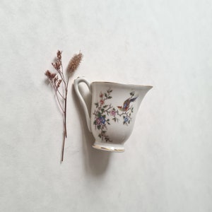 Peut inclure: Une crémier en porcelaine blanche avec un motif floral et un oiseau. La crémier a un bord doré et une poignée délicate.