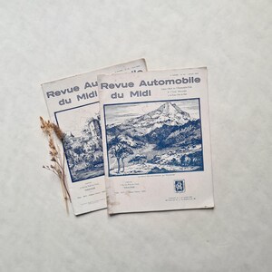 Peut inclure: Deux magazines français vintage intitulés "Revue Automobile du Midi" avec une illustration en bleu et blanc d'un paysage de montagne sur la couverture.