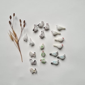 May include: A collection of miniature glass figurines of various animals, including cats, birds, and a dog. The figurines are white with painted details and are arranged on a white background.