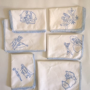 Puede incluir: Seis servilletas de lino blanco con dise&ntilde;os bordados en azul. Cada servilleta presenta una escena diferente, incluyendo una pareja sentada en un sof&aacute;, una pareja en un barco, una pareja en una rama de &aacute;rbol, una pareja bailando, una pareja a caballo y una pareja en un coche.