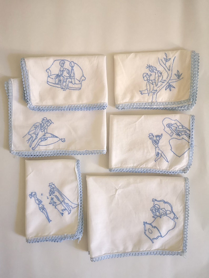 Puede incluir: Seis servilletas de lino blanco con dise&ntilde;os bordados en azul. Cada servilleta presenta una escena diferente, incluyendo una pareja sentada en un sof&aacute;, una pareja en un barco, una pareja en una rama de &aacute;rbol, una pareja bailando, una pareja a caballo y una pareja en un coche.