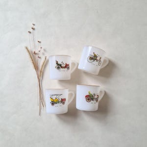 May include: Set of four white ceramic mugs with gold trim. Each mug features a vintage car illustration.