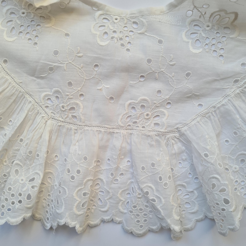 May include: White cotton lace trim with a scalloped edge and delicate floral embroidery. The lace has a ruffled bottom and is perfect for adding a touch of elegance to any project.