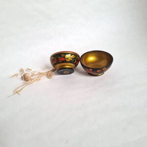Peut inclure: Deux petits bols noirs avec des motifs floraux peints en or et rouge. Les bols sont sur une surface blanche.