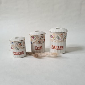 Puede incluir: Tres botes de cerámica blanca con diseños florales y detalles dorados. Los botes están etiquetados con "Farine", "Thé" y "Poivre".