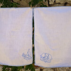 Puede incluir: Dos toallas de cocina blancas con dise&ntilde;os bordados en azul. Una toalla presenta un grupo de personas de pie, la otra presenta un grupo de personas sentadas en un sof&aacute;.