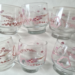 Pode incluir: Seis copos de vidro transparente com um design de paisagem rosa. O design inclui um barco, árvores e um edifício. Os copos têm uma forma arredondada e uma base espessa. O tema geral é vintage ou retro.