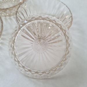May include: Close-up of several clear glass bowls. The bowls have a diamond pattern on the sides and a starburst design on the bottom. The bowls are likely for serving desserts or small portions.