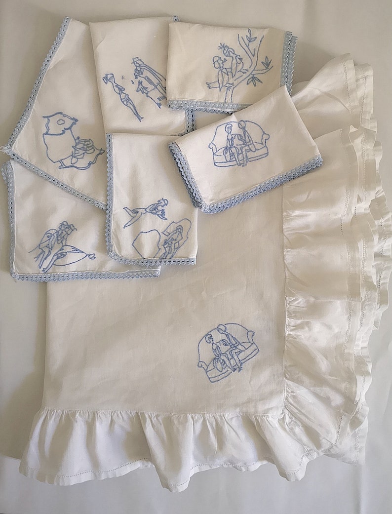 Puede incluir: Conjunto de siete servilletas de lino blanco con dise&ntilde;os bordados en azul. Cada servilleta presenta un dise&ntilde;o diferente, incluyendo p&aacute;jaros, una pareja sentada en un sof&aacute; y una pareja de la mano. Las servilletas tienen un delicado borde de encaje.