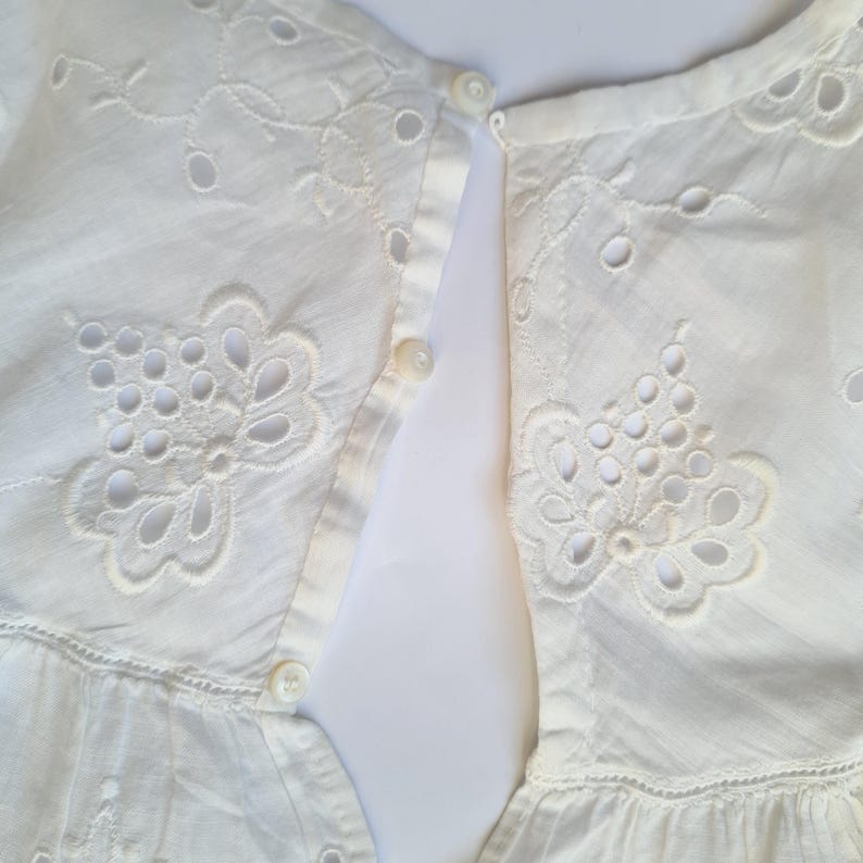 May include: White cotton dress with eyelet embroidery and a button closure in the back.