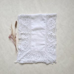 Peut inclure: Nappe en coton blanc avec une bordure en dentelle délicate. La dentelle est un motif floral sur fond blanc.