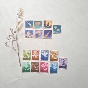 Peut inclure: Une collection de timbres-poste vintage représentant l'exploration spatiale et des personnalités historiques. Les timbres présentent des fusées, des planètes et des portraits dans diverses couleurs, dont le bleu, le vert et le violet. Les timbres sont disposés sur une surface blanche.