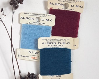 May include: Three spools of embroidery floss with labels that read "Dollfus-Mieg & Cie" and "Alson D.M.C." The spools are burgundy, light blue, and teal. The labels also include the text "A Repriser" and the number of meters and yards of floss on each spool.
