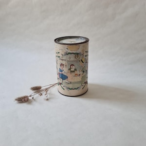 May include: A vintage tin can with a cream background and colorful illustrations of three children having tea. The can has a brown lid and is decorated with green leaves and flowers.