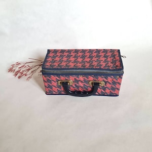 May include: A red and black patterned vintage suitcase with a black handle and brass accents.