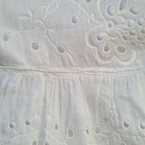 May include: White cotton fabric with a delicate eyelet pattern. The fabric has a ruffled edge and is perfect for a summer dress or blouse.
