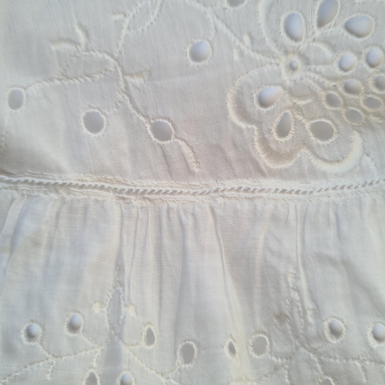 May include: White cotton fabric with a delicate eyelet pattern. The fabric has a ruffled edge and is perfect for a summer dress or blouse.