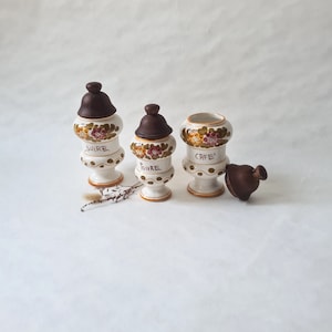 Peut inclure: Trois pots en céramique avec des motifs floraux et des couvercles marrons. Les pots sont étiquetés "Sucre", "Poivre" et "Café".