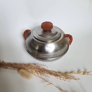 Peut inclure: Un sucrier en argent avec un couvercle et des poignées en bois. Le bol est rond et a une surface lisse et brillante. Le couvercle a un design simple et arrondi.