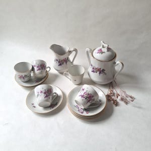Peut inclure: Service à thé en porcelaine blanche avec un motif floral rose et violet. L'ensemble comprend des tasses, des soucoupes, une crémière et une théière avec un couvercle, le tout avec des bordures dorées. Un service à thé classique.