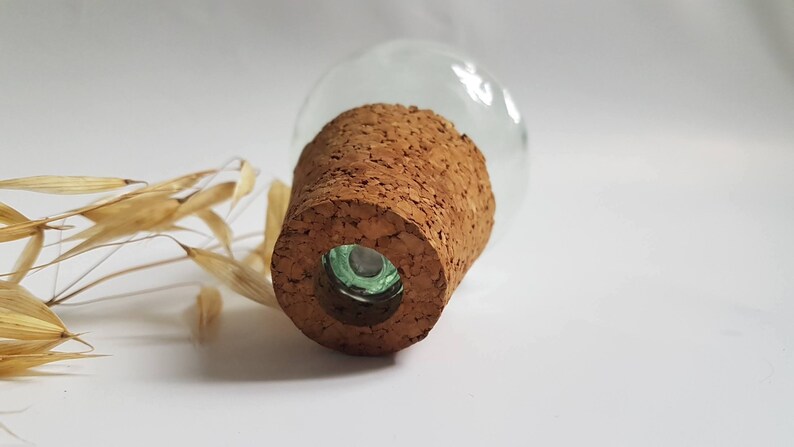May include: A clear glass bottle with a cork stopper. The cork is brown and has a rough texture. The bottle is sitting on a white surface.