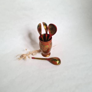 May include: Set of four hand-painted wooden spoons in a red and gold painted vase with floral designs. The spoons are red with gold accents and floral designs.