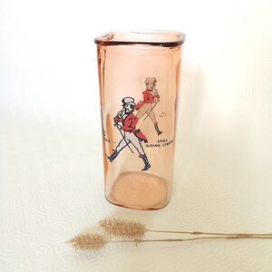 Peut inclure: Un verre &agrave; boire en verre rose avec une forme carr&eacute;e et une image imprim&eacute;e de deux hommes en v&ecirc;tements rouge et noir. Le texte "Still Going Strong" est imprim&eacute; sur le verre.