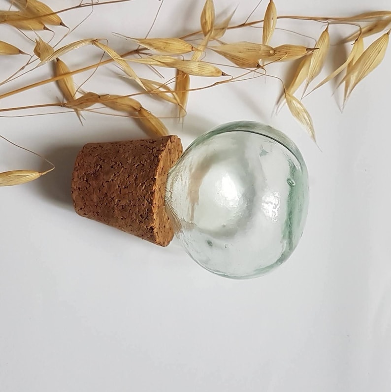May include: A clear glass bottle with a cork stopper. The bottle is round and has a smooth surface. The cork is brown and has a rough texture.